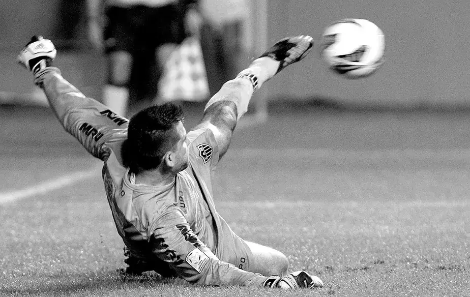 Victor, caído no gramado, desvia a bola com a perna